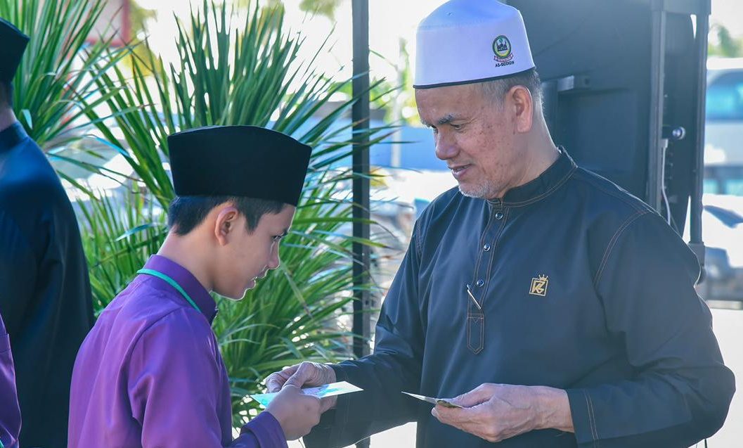 A young boy, dressed in purple, hands a slip of paper to an older man in a blue shirt and white turban.